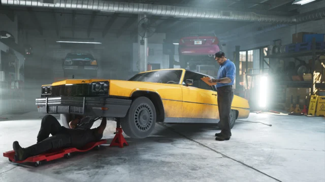 Um mecânico dentro da oficina Rideout Customs trabalha embaixo de um carro enquanto outro homem está parado perto do veículo.