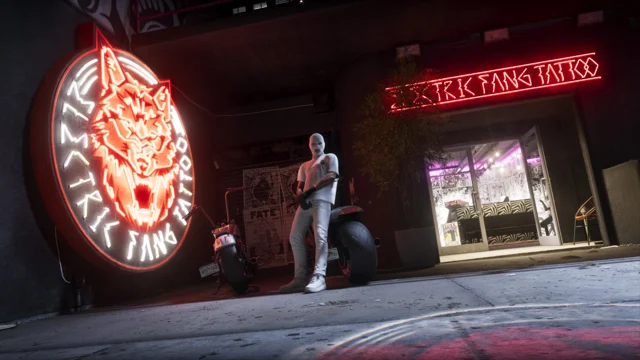 A neon Electric Fang Tattoo sign with a wolf reflects onto the asphalt at night.
